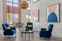 Chic and vibrant living space with plush blue chairs, modern art decor, and ample natural light through tall windows, offering a stylish and inviting atmosphere.