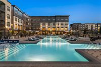 Luxurious apartment complex with a sparkling outdoor pool featuring stylish lounge chairs and illuminated modern architecture.