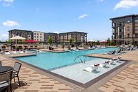 Modern apartment community with a luxurious swimming pool area featuring stylish lounge chairs, surrounded by beautifully designed multi-story buildings and vibrant landscaping.