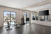 Modern fitness room with stationary bikes, wall mirrors, and large windows overlooking a swimming pool and residential buildings.