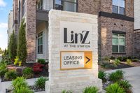 Inviting entrance to LinZ at the Station with a stylish leasing office sign amidst beautifully landscaped greenery.