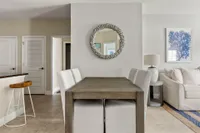 Modern dining area with elegant wooden table, plush chairs, and a stylish wall mirror, adjacent to cozy living room.