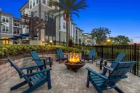 Outdoor fire pit with blue wooden chairs surrounding it in the nighttime with apartments in the background