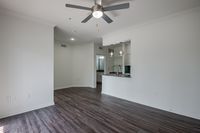 Chic living space with sleek hardwood floors, modern ceiling fan, and open kitchen area featuring stylish pendant lighting.