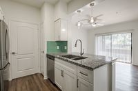 Modern kitchen with elegant granite countertops, sleek stainless steel appliances, and chic pendant lighting, leading to a bright living area with large glass doors.