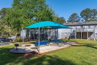 Charming outdoor space with vibrant blue picnic tables under a shade sail, perfect for gatherings in a lush green setting.