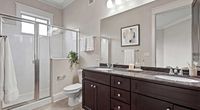 Modern bathroom with sleek dark wood cabinetry, elegant double sinks, and a spacious glass-enclosed shower, accented by stylish decor and natural light.