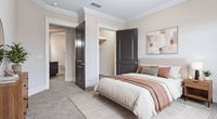 Inviting bedroom with elegant decor, featuring a cozy bed with earth-toned pillows and throws, modern art, and sleek wooden furniture.