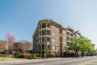 Charming brick apartment building with elegant balconies and lush landscaping, situated on a vibrant city street under a clear blue sky.