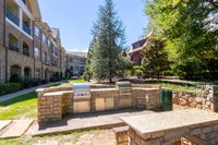 Charming apartment courtyard featuring elegant stone architecture and a modern outdoor grill area surrounded by lush greenery and scenic views.