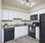 Bensalem Apartments - Village Square - An Updated Kitchen With Wood-Style Flooring, White Cabinetry, And Modern Black Appliances