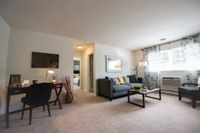 Pet-Friendly Apartments In West Chester, PA - Open Floor Living Room With Carpet Flooring, Large Window With Blinds, And Access To Bathroom And Bedroom.