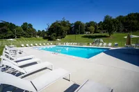 One-Bedroom Apartments in Bethel Park, PA - Lindenbrooke - Swimming Pool with Expansive Sundeck, Lounge Chairs, Tables and Chairs with Umbrellas, and Surrounding Manicured Landscape.