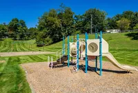 Dog-Friendly Apartments in Bethel Park, PA - Lindenbrooke - Playground with Wood Chips-Covered Surface, Jungle Gym with Slide, Swing Set, and Surrounding Manicured Landscape.