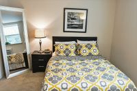 Cozy bedroom featuring a stylish bed with yellow and gray patterned bedding, a nightstand with a lamp, and a large mirror.