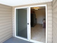 View of a modern kitchen through a sliding glass door from a patio area with beige siding.
