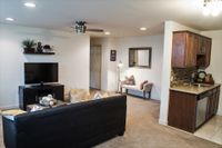 Inviting open-concept living room with cozy seating, modern TV setup, and elegant kitchen corner, perfect for relaxation and social gatherings.