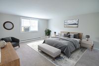 Elegant bedroom with a plush bed, stylish decor, cozy seating, and large window letting in natural light.