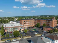 Aerial view of a charming brick apartment building with ample parking, surrounded by lush greenery and clear blue skies.