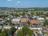 Charming aerial view of urban neighborhood with vibrant greenery and historic brick buildings, offering scenic living in a picturesque setting.