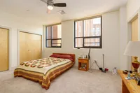Bright and spacious bedroom featuring large windows, cozy bed with a quilted cover, and ample closet space.