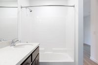 Modern bathroom with sleek white tiles, elegant vanity, and curved shower rod in a spacious apartment.