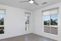 Bright bedroom with large windows and wood flooring, offering a serene view of palm trees.