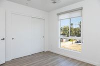 Bright, minimalist room with wood flooring, large window offering a serene view, and spacious closet.
