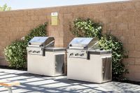 Outdoor cooking station featuring modern stainless steel grills set against a stylish brick wall with lush greenery.