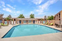 Inviting apartment complex with a sparkling outdoor pool, comfortable lounge chairs, and charming architectural details under a bright blue sky.