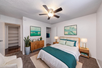 Elegant bedroom featuring modern decor with a plush bed, stylish wooden furniture, and calming green artwork, accentuated by ample natural light and a ceiling fan for comfort.
