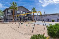 Inviting apartment courtyard with modern swing set, lush palm trees, and sunny skies.