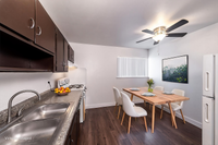 Chic kitchen with modern dark cabinets, dual sink, and elegant dining area featuring a wooden table and plush chairs, enhanced by ambient ceiling fan lighting.
