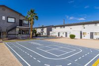 Charming apartment complex with a modern sports court and palm tree, offering a vibrant community atmosphere under blue skies.