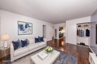 Modern living room with elegant white sofa, navy cushions, and sophisticated wall art, leading to a sleek kitchen and featuring rich hardwood floors with a cozy, upscale atmosphere.