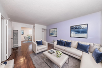 Chic living room with elegant white sofas accented by blue cushions, featuring a beautiful pastel wall and contemporary art, leading into a bright dining area.