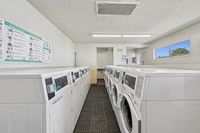 Bright and modern apartment laundry room with rows of white washers and dryers, spacious layout, and natural lighting from large windows.