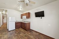 Inviting apartment kitchen with elegant wood flooring, sleek white appliances, rich cabinetry, and a mounted flat-screen TV.