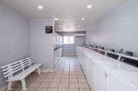 Modern and bright communal laundry room featuring multiple washing machines, tiled floors, and a cozy white bench under soft lighting.
