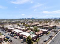 Aerial view of a vibrant apartment complex with palm tree-lined streets, ample parking, and a glimpse of the city skyline under a clear blue sky.