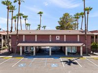 Inviting two-story residential building with a charming red tile roof surrounded by tall palm trees, featuring accessible parking spaces under a clear blue sky.