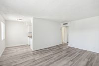 Bright and airy open living space with modern hardwood floors, inviting natural light through large windows, and a glimpse of the sleek kitchen area.