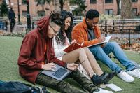 three people sitting in grass and studying