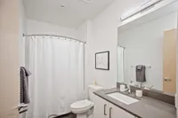 Downtown Portland OR Apartments - ORO - Bathroom With High Ceilings, Wood-Style Flooring, Large Vanity Mirror, Quartz Countertops, Toilet, And A Shower/Tub Combo.