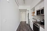 Studio Apartments in Downtown Portland OR - ORO - An interior shot of the kitchen featuring Stainless Steel Appliances, Grey Countertops, White Cabinetry, Wood-Style Flooring, and Tile Backsplash