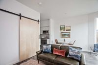 Modern Apartments in Downtown Portland, OR - ORO - Furnished Living Room With Wood-Style Floors, Barn-Style Sliding Door, A Large Window, A Dining Area, And A Kitchen With Stainless Steel Appliances