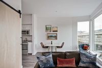 Downtown Portland, OR Luxury - ORO - ApartmentsLiving Room With Wood-Style Flooring, High Ceilings, Large Windows, A Brown Leather Sofa, And A Dining Area With A 2-Person Table