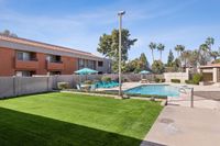 Pool with lounge chairs, sun, bushes, grass, and table and chair sets