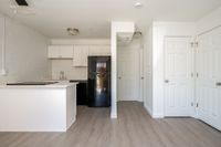 Kitchen and living area with fridge, counters, sink, cupboards, wooden floors, and doors.
