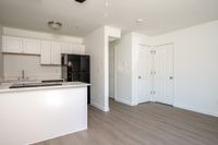 Kitchen and living area with fridge, counters, sink, cupboards, wooden floors, and doors.